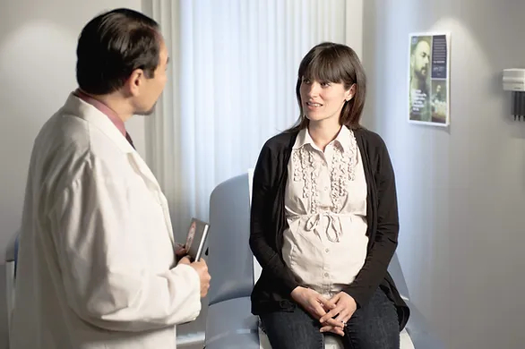 pregnant woman sitting on table talking to doctor - choosing an obgyn