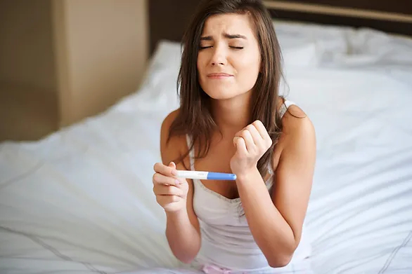 woman closing her eyes holding a pregnancy test - Is 7 DPO Too Early to Take a Pregnancy Test