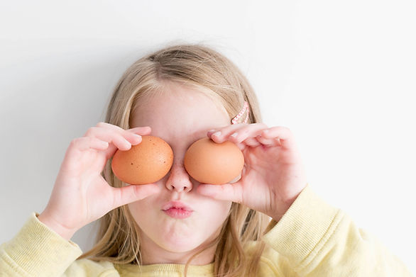 young girl holding two brown eggs up to eyes