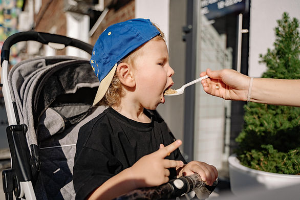 picky eater - child being fed with a spoon while sitting in a stroller and wearing a baseball cap backwards