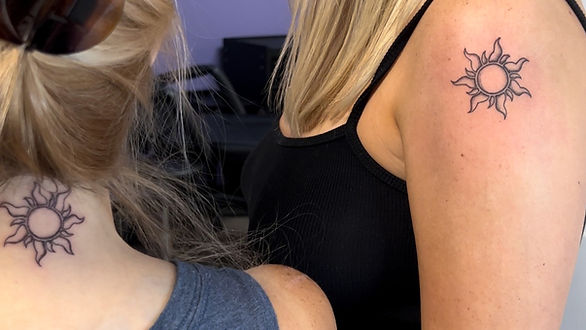 styles of tattoos - back of woman's neck with sun tattoo outline, next to girl standing with arm showing the identical sun tattoo