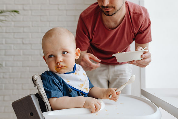 picky eater - dad trying to feed baby in high chair with child looking away