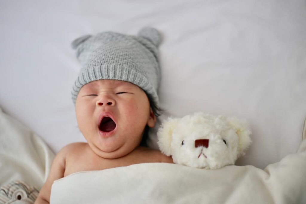 baby yawning with cap on; sleep training