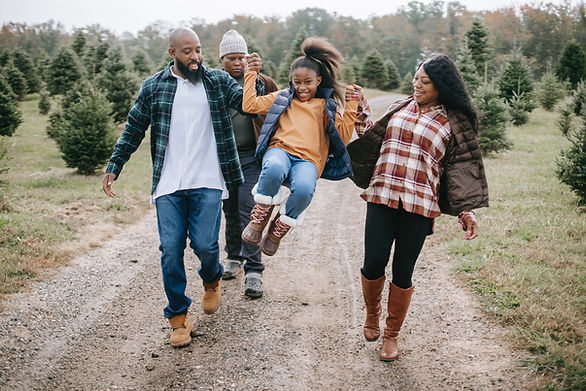 dark skinned family of four walking down a path, mom and dad swinging 8 year old daughter 