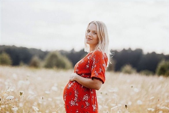pregnant woman holding belly and smiling in a field - pregnancy common questions