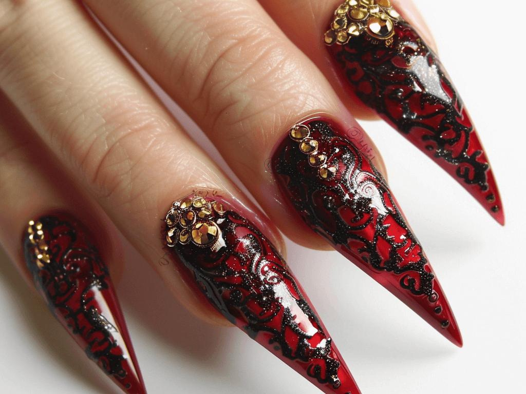 Elegant stiletto-shaped mob wife nails with a deep red glossy finish, adorned with gold rhinestones and tiny black lace patterns.