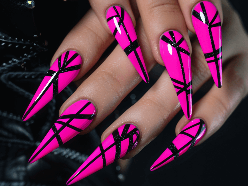 Bold neon pink mob wife nails in a long, stiletto shape, adorned with contrasting black geometric patterns and tiny gemstones.