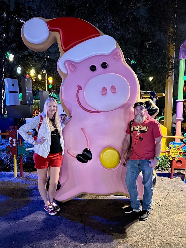 woman standing on left, man standing on right, large iced sugar cookie Christmas pig in the middle. Disney Toy Story Ham. 