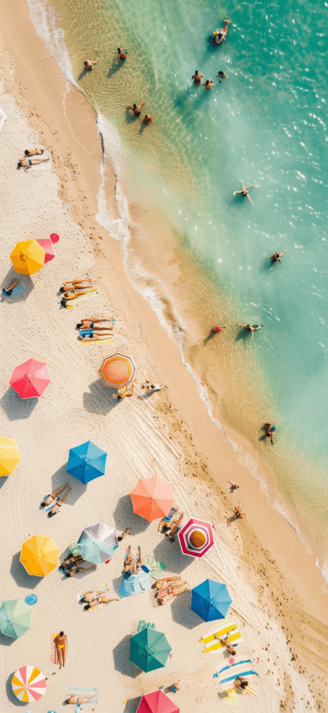 An aerial view of a sandy beach dotted with colorful umbrellas and sunbathers enjoying the clear, sunny day. This image brings a sense of bustling beach life and vibrant summer fun. Summer iPhone wallpaper.