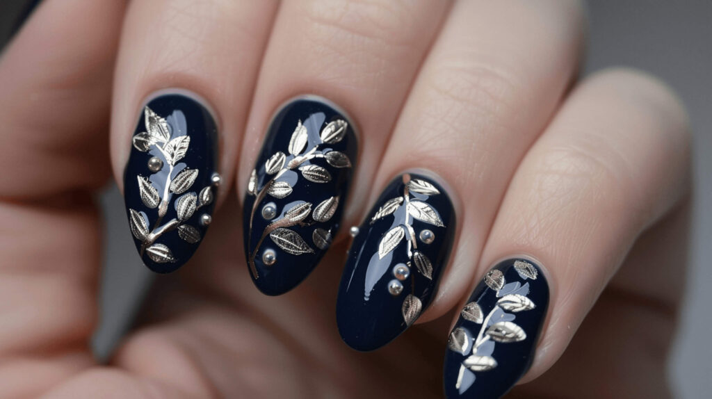 A set of nails painted in deep navy blue with fine, silver olive leaves and tiny owl designs, reflecting the wisdom and war attributes of the goddess Athena. 