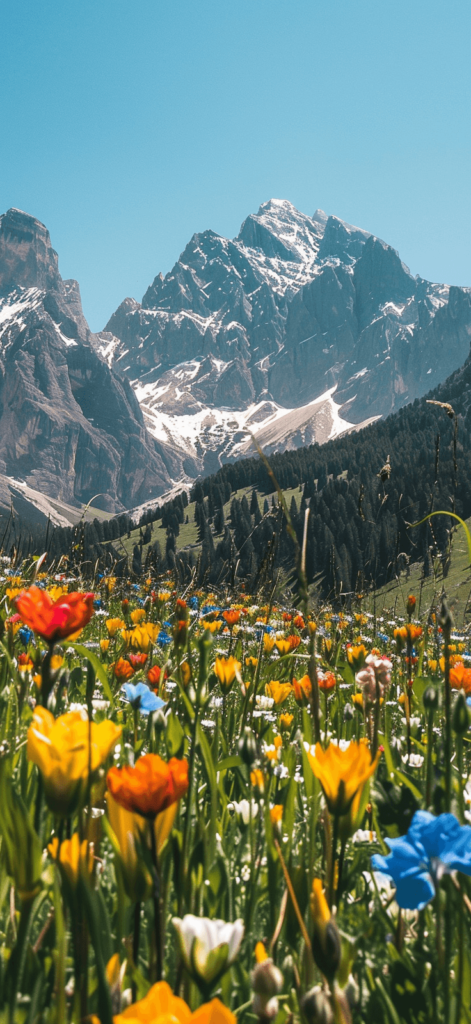A picturesque mountain landscape with wildflowers in the foreground under a clear blue sky.