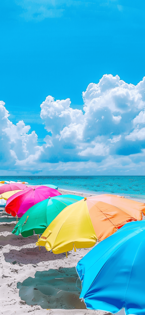 Colorful beach umbrellas lined up on the sand, with a bright blue sky and a glimpse of the ocean in the background.