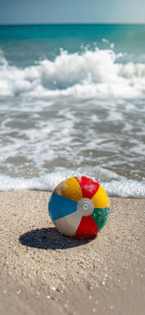 A playful beach ball on the sand with gentle waves in the background. Summer wallpaper. 





