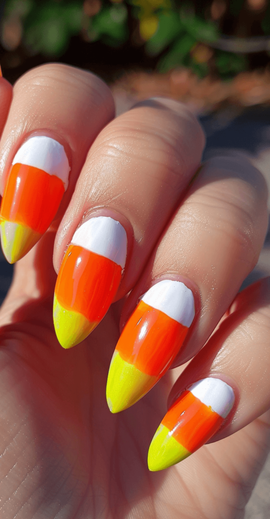 Nails painted in a candy corn pattern with orange at base of nail, yellowin the middle, and white tips in an ombre stripe pattern.