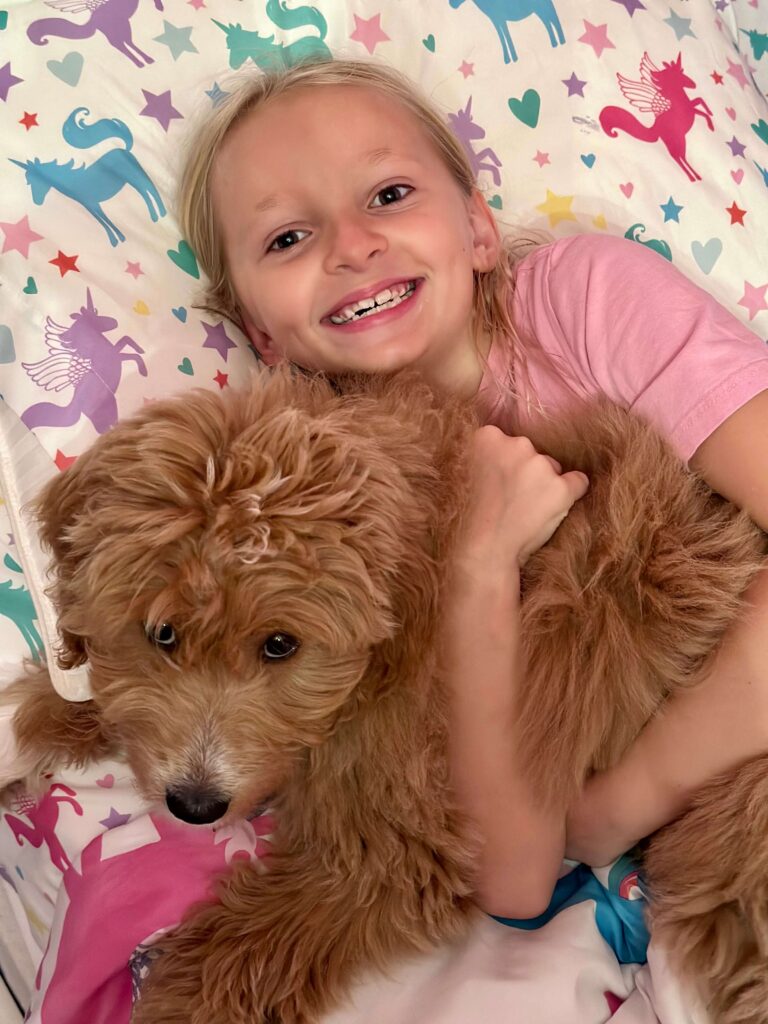 girl laying down hugging her Goldendoodle family dog