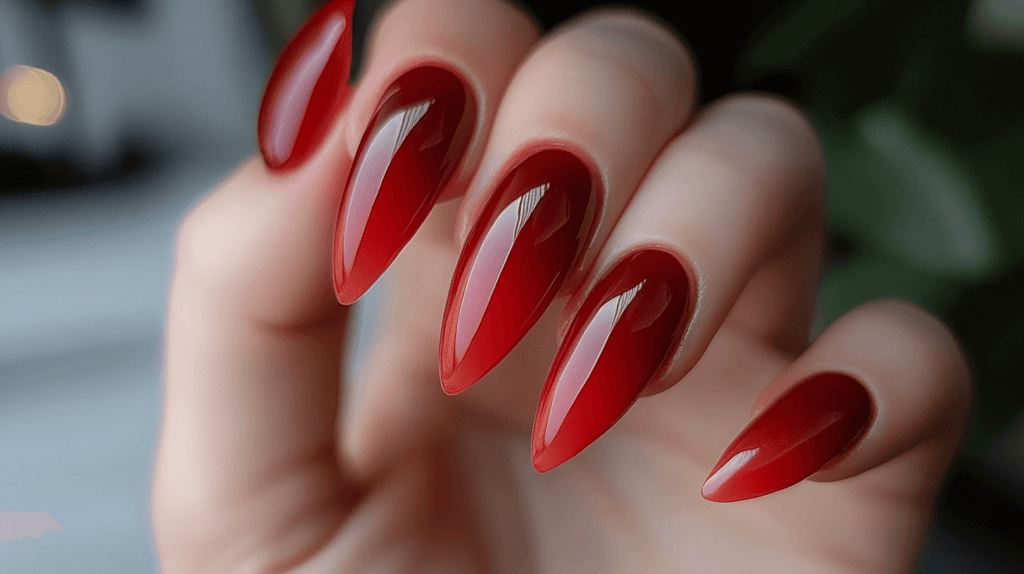 A classic red manicure on a female hand, nails are long and almond-shaped.





