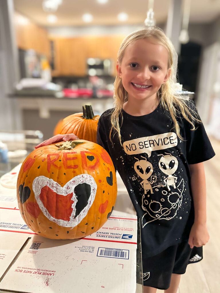 girl next to a painted pumpkin