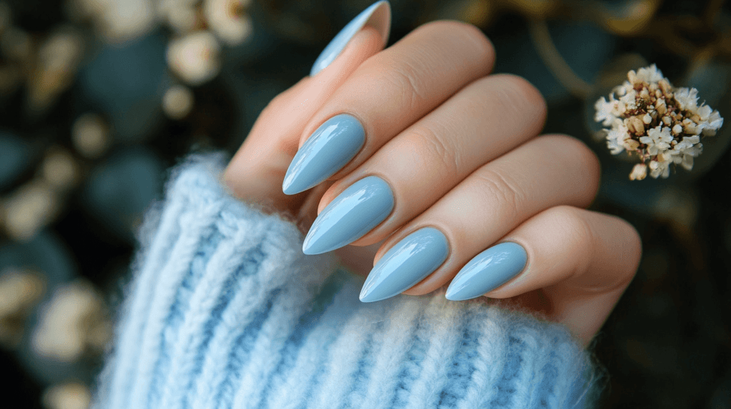 A pale blue manicure on a female hand, nails are almond-shaped and polished.
