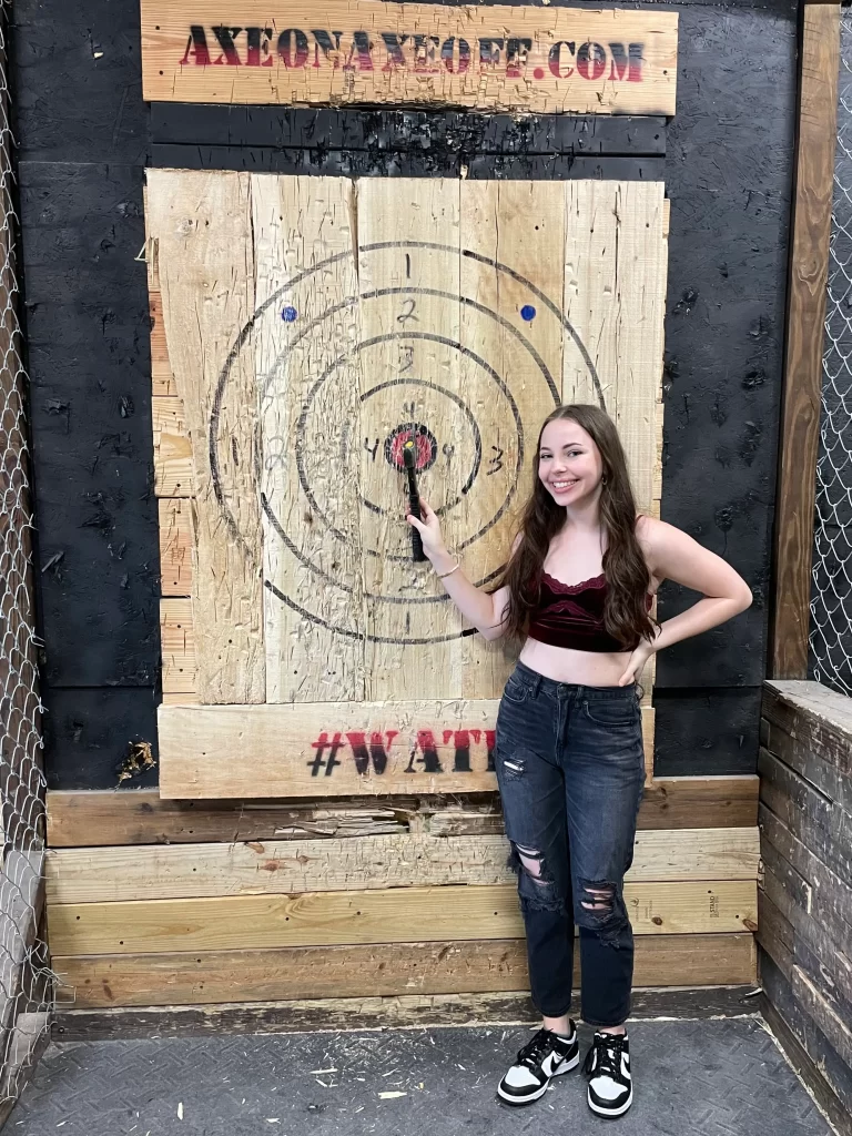 girl standing in front of an axe throwing board with an ax