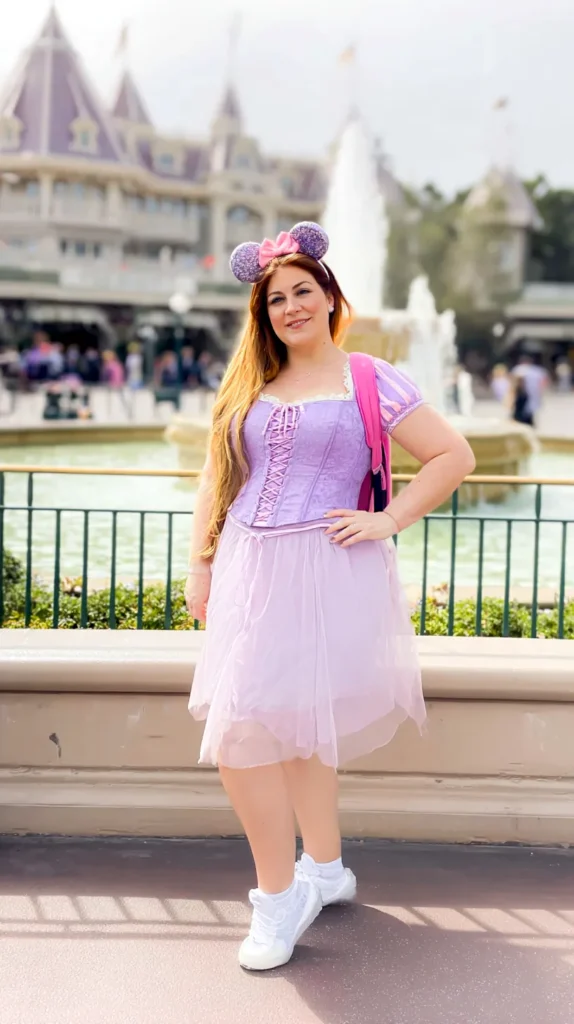 Adult woman in a themed outfit posing near a castle with a blurred park background.