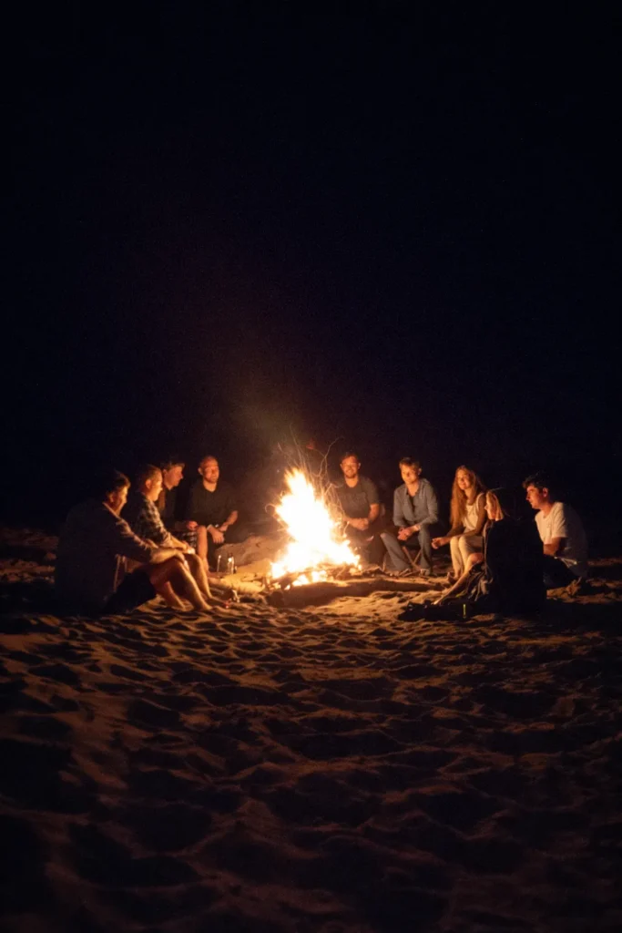 people crowded around a bonfire on the beach