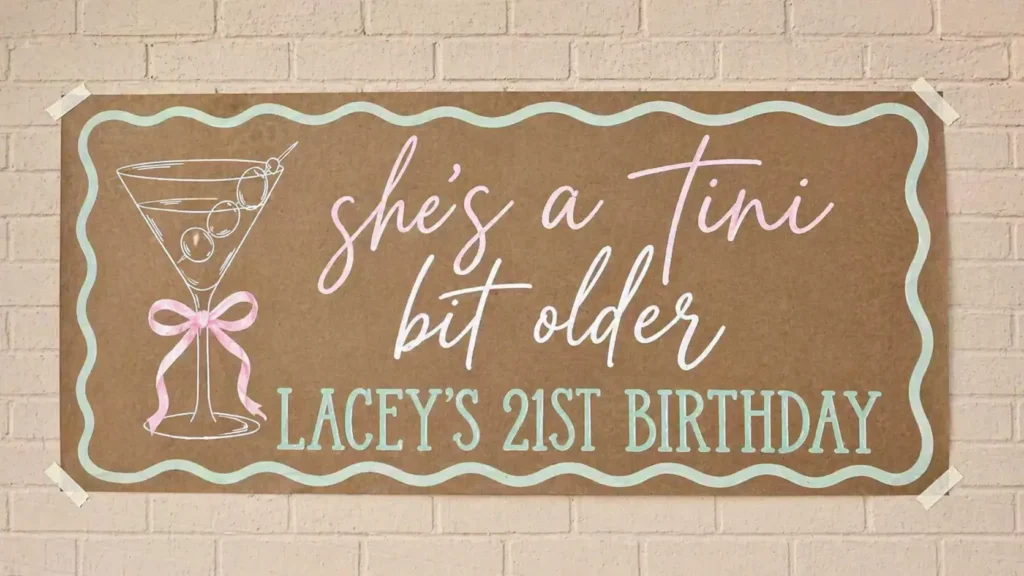 Handmade brown birthday banner taped to a light brick wall with a martini glass illustration and pastel lettering that reads “she’s a tini bit older, Lacey’s 21st birthday.”