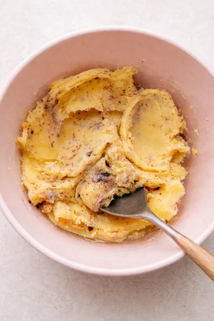 Overhead view of chilled brown butter in a light pink mixing bowl, scoopable and speckled with toasted brown milk solids.