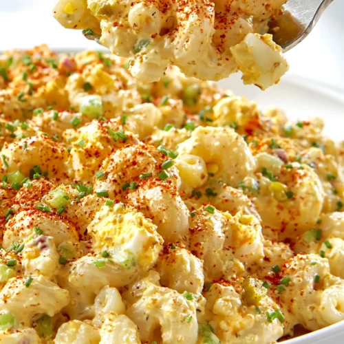 Fork lifting a creamy bite of deviled egg pasta salad with elbow macaroni, egg, celery, and paprika.