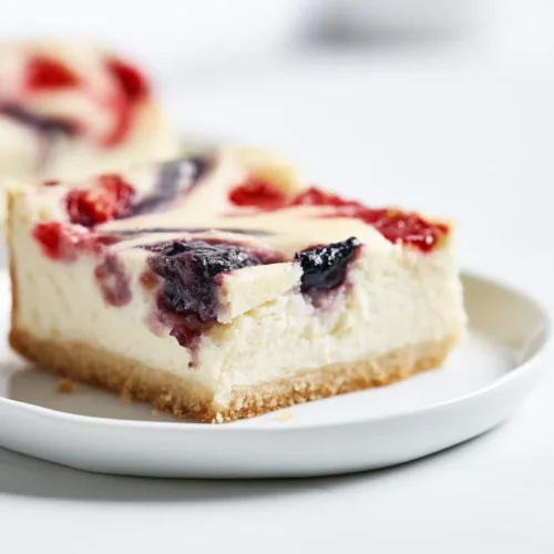 hick but homemade cheesecake cookie bars cut from a 9x13 pan, pale golden sugar cookie crust, creamy white cheesecake filling, light strawberry jam and blueberry preserve swirls mostly on top with a little marbling inside, realistic homemade edges, not bakery-perfect, one bar on a white plate with one additional bar beside it, white marble counter, bright white kitchen, natural window light