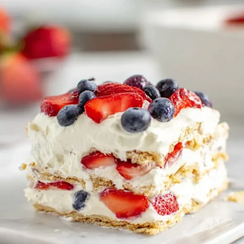 hyper-realistic photo of a square slice of no-bake berry icebox cake with 2 visible graham cracker layers, 2 layers of fluffy white cream filling, sliced strawberries and whole blueberries between the layers, and a smooth cream topping with extra berries on top, set on a white marble kitchen counter in a bright white kitchen, crisp natural window light, airy editorial dessert photography, realistic textures and proportions, no people, no hands, no text, no watermark