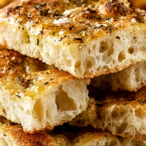 hyper-realistic close-up photo of sliced focaccia bread squares stacked casually on a white ceramic plate, crisp golden crust, soft airy interior with large bubbles, glossy olive oil sheen, rosemary bits and flaky salt on top, bright white lighting, minimal shadows, cozy kitchen counter, no people, no hands, no text