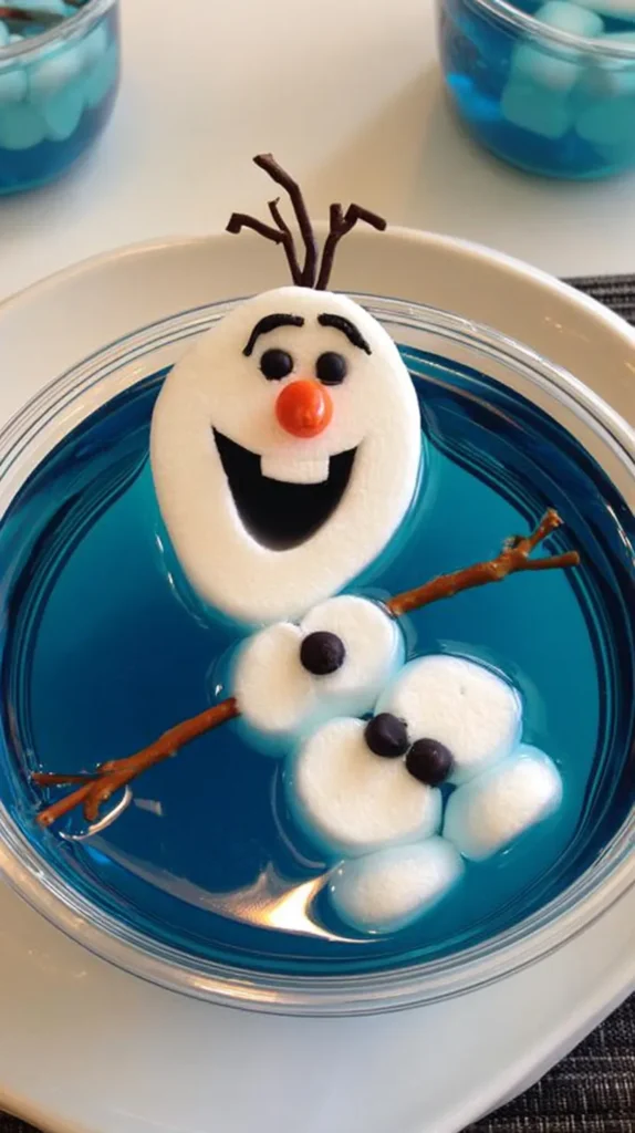 Cute marshmallow Disney's OLAF snowman dessert floating in a clear cup of bright blue Jello, inspired by a cheerful animated snowman look, made from white marshmallows with a large long head, smaller round body pieces, big happy open smile, black candy eyes, arched black eyebrows, small orange carrot-shaped candy nose, tiny black candy buttons, thin pretzel stick arms, three twig-like chocolate hair pieces, playful tilted pose, glossy blue gelatin, clear plastic dessert cup, clean white tabletop, one or two matching dessert cups softly blurred in the background, bright kid-friendly party food photography, crisp realistic edible textures, whimsical frozen pool party dessert, no text, no watermark