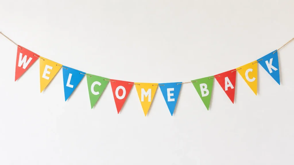 Colorful bunting banner strung across white wall spelling "Welcome Back" in red, yellow, blue, and green triangular flags