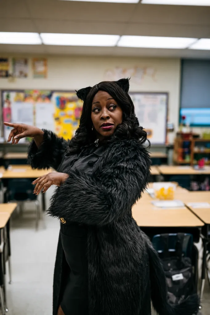 Woman wearing black cat costume with ears and fur in a classroom, gesturing expressively during a lesson