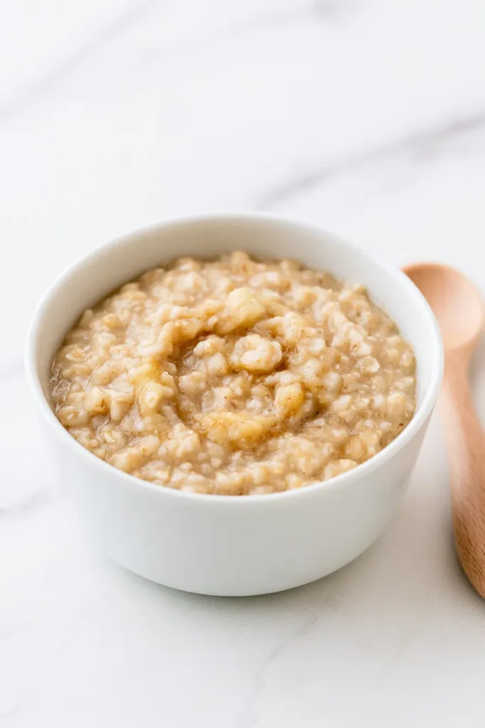 Creamy oatmeal cereal in a white bowl with a wooden spoon on a marble surface