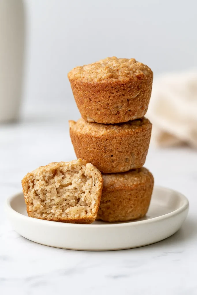 Stack of three homemade whole grain muffins on a white plate with one cut in half to show the fluffy interior crumb