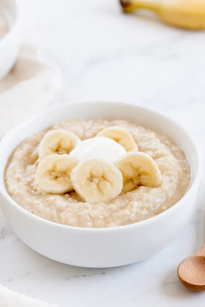 Creamy oatmeal cereal in a white bowl topped with banana slices and yogurt